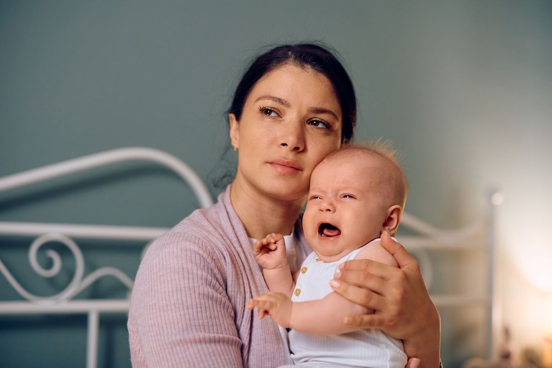 Young Mother Holding Her Crying Baby At Home